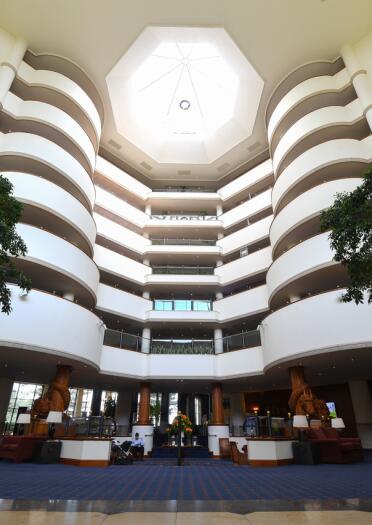 A large atrium in a hotel with a glass sunlit roof and trees.